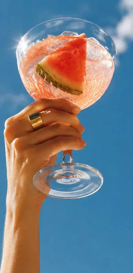 A hand raising an Easy Landings watermelon cocktail against a bright blue sky