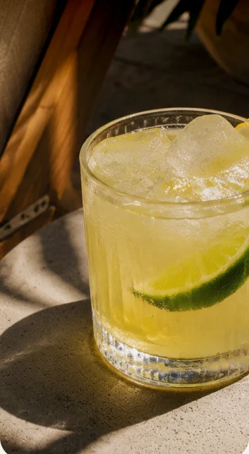 A lime cocktail in a tumbler on a sunlit table