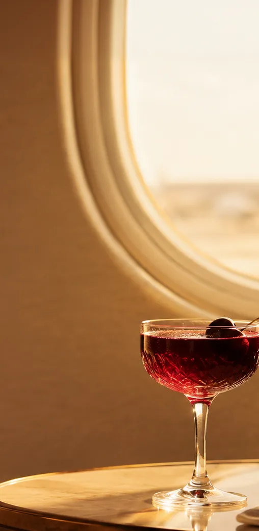 A dark cherry cocktail on a table by a sunlit aircraft window